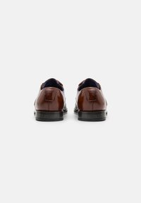 Bruine leren jurk schoenen met een gladde afwerking, ronde vorm, contrasterende interieurkleur en lage zwarte hakken.