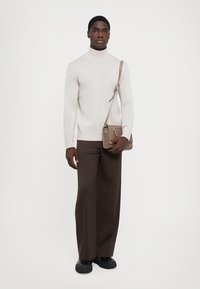 Pullover a collo alto beige chiaro, pantaloni a gamba larga marroni e scarpe nere. Include una piccola borsa a tracolla in una tonalità tenue.