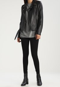 Schwarze Leder-Motorradjacke mit Reißverschlusstaschen, graues strukturiertes Oberteil, schwarze Skinny-Jeans und Stiefeletten mit Absatz und Reißverschluss-Details.