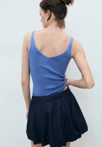 Blue knit tank top with a V-back, paired with a dark denim flared skirt. The fabric appears soft with a subtle ribbed texture.