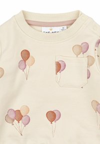 Sudadera de color beige claro con estampados de globos en tonos pastel. Cuello acanalado con dos botones a presión y un pequeño bolsillo en el pecho. Textura suave.