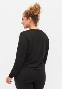 Crna majica dugih rukava s okruglim izrezom. Dizajnirana za opušteni fit, ima glatku, rastezljivu tkaninu i minimalne šavove na leđima.