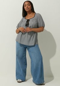 Blusa a quadri bianca e nera con scollatura quadrata, maniche a sbuffo corte e davanti con coulisse, abbinata a jeans in denim blu a gamba larga.