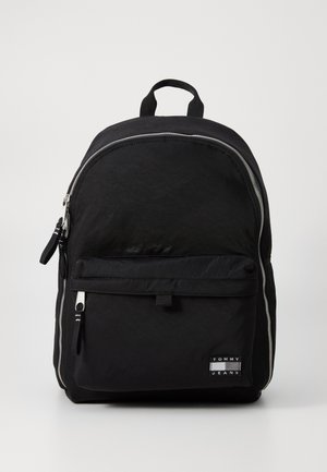 Black nylon backpack with a smooth texture, silver zippers, front pocket, and a small logo patch. Dual carry handle and adjustable straps.