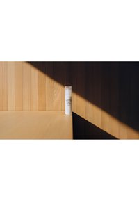 Bouteille de crème solaire étiquetée "Susanne Kaufmann SPF 50" posée sur une surface en bois avec des contrastes marqués de lumière et d'ombre.