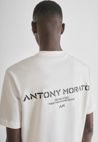 Camiseta blanca de algodón con mangas cortas. El texto en la parte posterior dice "ANTONY MORATO ESTABLISHED TWO THOUSAND SEVEN" en negrita, en color negro.