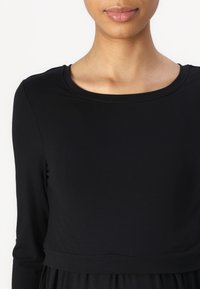 Svart l ångärmad topp med rund halsringning. Slät tyg med en figurnära överdel och en lös nedre del, vilket skapar en avslappnad silhuett.