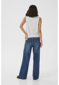 Grijze mouwloze top gecombineerd met wijde blauwe jeans. De denim heeft achterzakken en een comfortabele pasvorm. Eenvoudig ontwerp zonder zichtbare patronen.