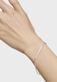 Bracciale d'argento su un polso, caratterizzato da un design delicato a catena con maglie a forma di fiore e una finitura fine e lucida.