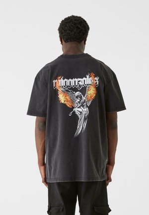 Black oversized t-shirt made of cotton, featuring a graphic print of a winged figure with flames and stylized text on the back.