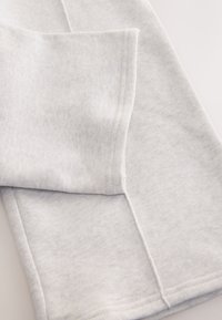 Gros plan d'un tissu gris clair doux avec des lignes de couture visibles et un bord plié, montrant la texture et les détails de couture.