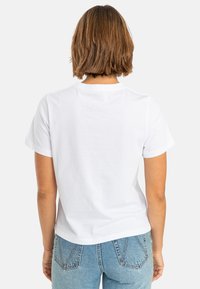 White cotton t-shirt with short sleeves and a crew neckline, displayed from the back, paired with light blue denim jeans.