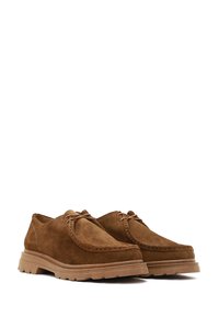 Brown suede shoes featuring a rounded toe, decorative stitching, and a thick, textured sole with grooves for grip. Lace-up closure.