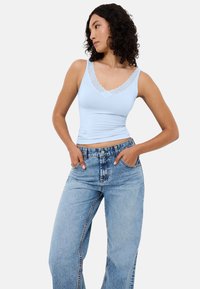 Light blue fitted tank top with a scalloped lace neckline, paired with high-waisted, faded blue denim jeans. Smooth fabric texture.