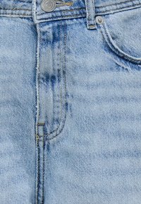 Primo piano di jeans in denim azzurro chiaro che mostra il bottone frontale, i passanti per la cintura e la tasca per le monete con cuciture e texture visibili.