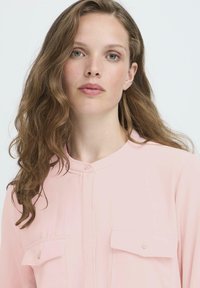 Helles rosa Bluse mit Kragen, Knopfverschluss und zwei Brusttaschen. Weicher Stoff mit glatter Textur und lockerem Schnitt.