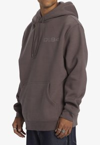 Grijze sweatshirt met capuchon, voorzak en een gestructureerde afwerking. Voorzien van een subtiel reliëf "Dc94" logo op de borst.