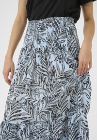 Blue skirt featuring a smocked waistband, adorned with a black and white leaf pattern, and tiered ruffles along the hem.