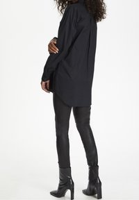 Sort langærmet skjorte med en lige skæring, parret med tætsiddende sorte læderbukser og skinnende hæle støvler. Glat stof med et enkelt design.