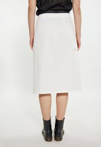 Witte midi rok met zijzakken, gladde textuur en een rechte snit. Gestyleerd met zwarte enkellaarsjes voor contrast.