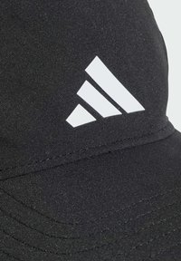 Black cap made of fabric with a smooth texture, featuring a large white Adidas logo and stitched accents for added detail.