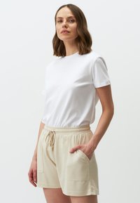 Witte korte mouwen t-shirt gecombineerd met beige shorts met touwtjes, voorzien van twee zijzakken en een zachte stoftextuur.