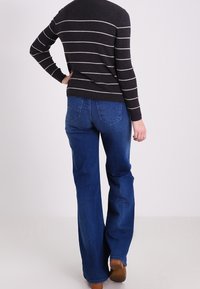 Pull en laine noir et blanc à rayures avec une texture côtelée, associé à un jeans en denim bleu évasé avec poches arrière et un lavage moyen.