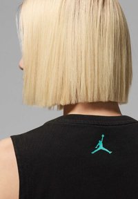Camisa sin mangas negra con un escote redondeado, que presenta un logo de Jordan en color verde azulado en la parte posterior. La tela parece suave con una textura lisa.