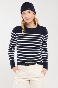 Maglione a righe blu navy con strisce orizzontali bianche, colletto rotondo e bottoni sulle spalle; abbinato a pantaloni beige e un berretto blu navy.