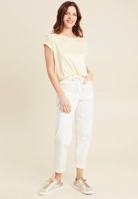 Gouden glinsterende top met korte mouwen, gecombineerd met witte, omgeslagen, elastische taillebroek en lichtgekleurde sneakers met gouden accenten.