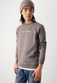 Pelēks sporta krekls ar ribotu apkakli un piedurknēm, ar baltu 'Marc O’Polo DENIM' logo. Saskaņots ar gaiši ziliem džinsiem.