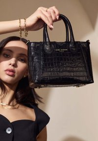 Zwarte handtas met krokodillenstructuur, korte handgrepen en gouden hardware. Heeft een rechthoekige vorm en een gladde, glanzende textuur.