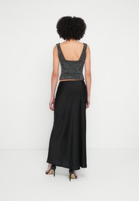 Črno satensko maxi krilo v kombinaciji s prilegajočo se, bleščečo kratko majico s kvadratnim hrbtom in širokimi naramnicami. Gladek tekstura, eleganten dizajn.