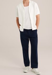 Vitt kortärmat texturerat skjorta med knappar, kombinerad med marinblå byxor och vita sneakers. Enkel, avslappnad design och ledig passform.