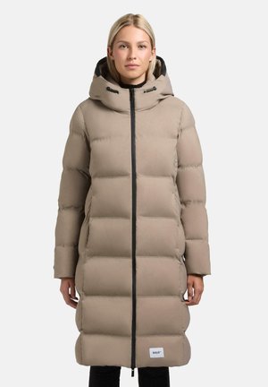 Lang beige pufferjakke med lynlås foran, stort hætte og elastiske manchetter. Har et syet mønster og et logo patch nær kanten.