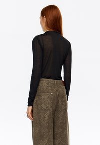 Czarna bluzka z długim rękawem o dopasowanym kroju, noszona z luźnymi oliwkowozielonymi spodniami z teksturowanym wzorem i dwoma tylnymi kieszeniami.