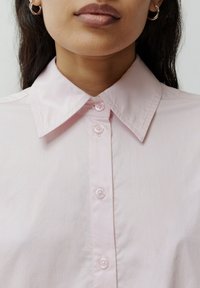 Helles rosa Hemd mit Kragen und durchgehender Knopfleiste, mit sichtbaren Knöpfen und einer glatten Textur. Die Kragen sind spitz und gleichmäßig.