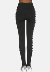 Czarne legginsy z wysokim pasem, ozdobione białymi bocznymi panelami w panterkę oraz gładką, elastyczną teksturą. Noszone z szarymi sneakersami.