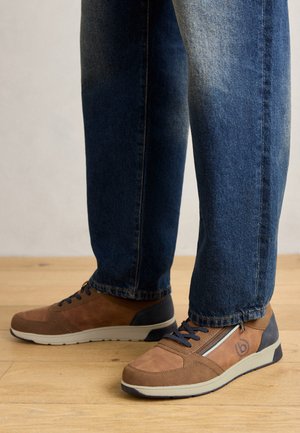 Chaussures en daim brun et textile avec accents bleus, bout rond, lacets et détail de fermeture éclair. Portées avec un jean en denim bleu sur un sol en bois.