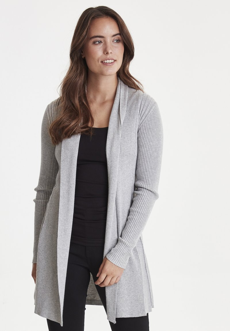 Cardigan grigio a coste con maniche lunghe e design aperto, abbinato a un top nero aderente, su uno sfondo bianco semplice.