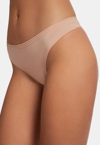 Beige ondergoed met een zachte textuur, met een low-rise ontwerp, delicate stiksels en minimale bedekking. Zachte afwerking op de randen.