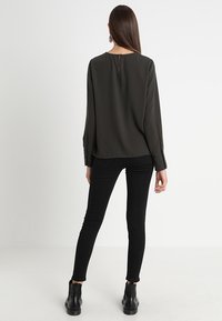 Dark green blouse with a rounded back neckline and button closure, paired with black slim-fit jeans and black ankle boots.