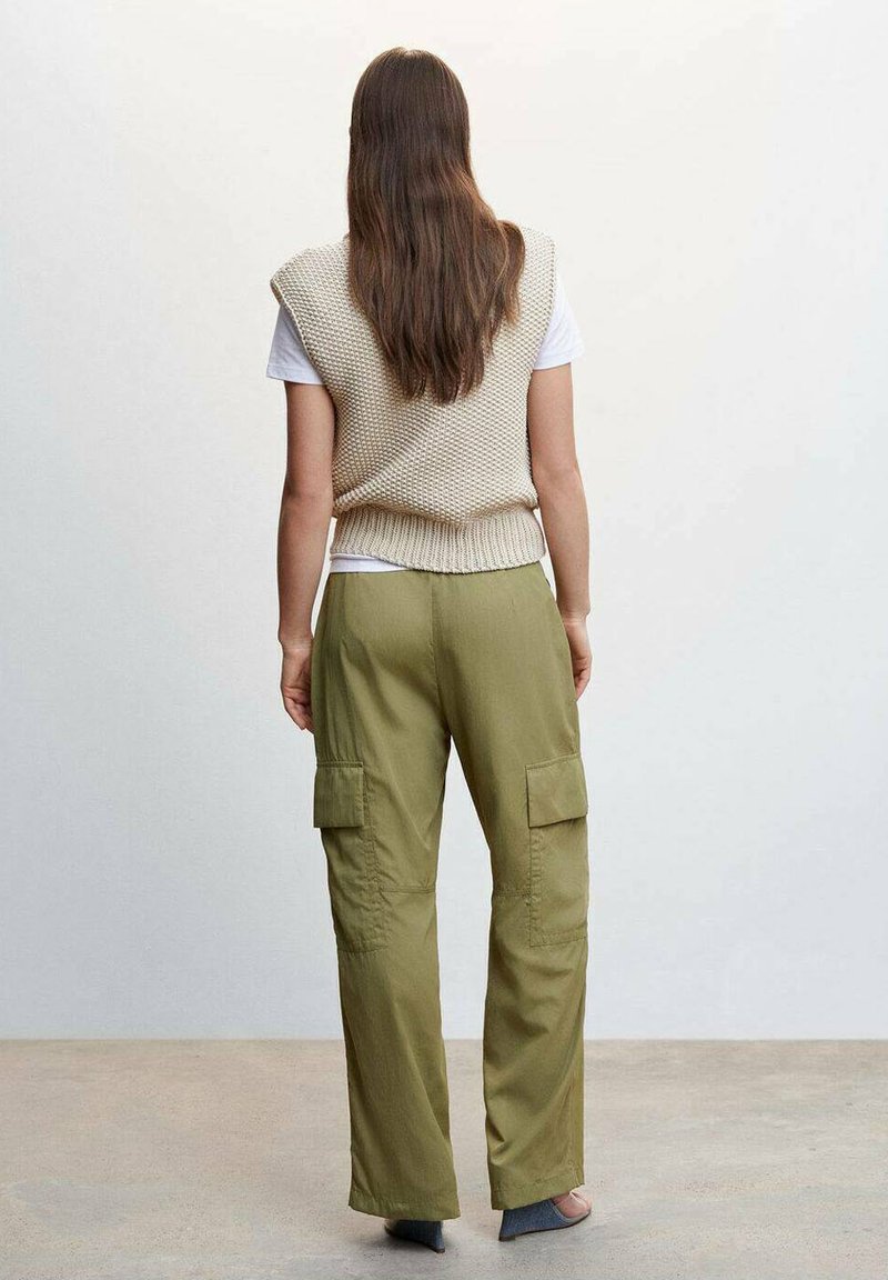 Beżowa dzianinowa kamizelka na białej koszulce, w połączeniu z zielonymi spodniami cargo z bocznymi kieszeniami. Gładki i luźny krój.