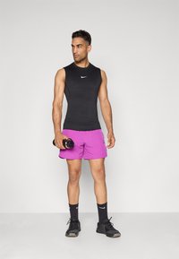 Black sleeveless athletic top, purple shorts with black logo, black ankle socks, and black athletic shoes, holding a black dumbbell.
