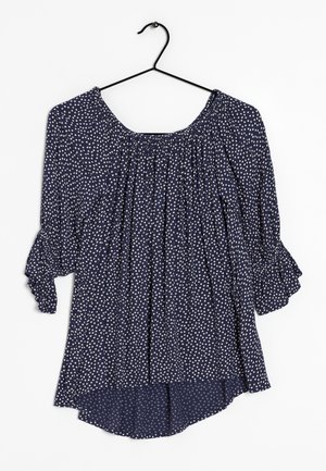 Marinebluse med hvide polkaprikker, elastisk halsudskæring, trekvartærmer med flæser og en asymmetrisk kant. Lavet af letvægtsstof.