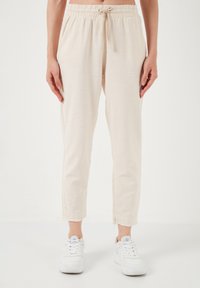 Light beige, lightweight pants with an elastic waistband and drawstring. Tapered fit with frayed hem. Paired with white sneakers.