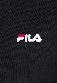 Svart ribbat tyg med en framträdande vit "FILA"-logotyp med en röd accent, placerad diagonalt.