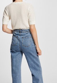 Suéter de punto color crema de manga corta con un patrón texturizado, combinado con unos jeans de cintura alta de color azul claro con un corte relajado y bolsillos traseros.