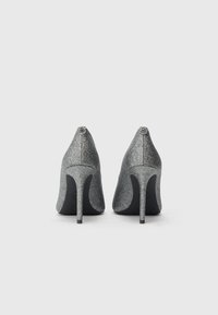 High-heeled shoes in silver glitter with a pointed toe design. Sleek silhouette with black soles and small branded accents on the heels.