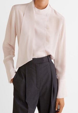 Vaaleanpunainen pitkähihais blouse, jossa on korkea kaulus ja laskostettu läppä, yhdistettynä korkeavyötäröisiin, tummanharmaisiin mittatilaustyönä tehtyihin housuihin.